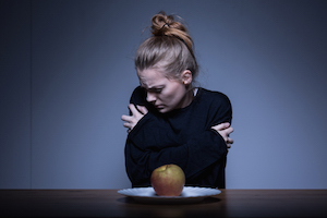 Ung kvinde væmmes over et æble på tallerkenen foran hende for at signalere sin spiseforstyrrelse 