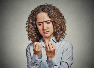 Kvinde med krøllet mørkt hår iført en lyseblå skjorte, kigger frustreret på sine ned-spiste negle