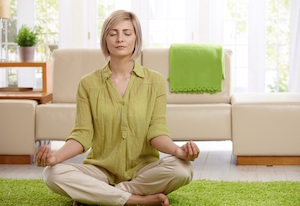 Dame sidder i meditativ stilling på et grønt tæppe iført grøn skjorte i sin stue 