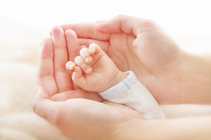 Nybagt mor holder sit nyfødte spædbarns hånd i sine hænder